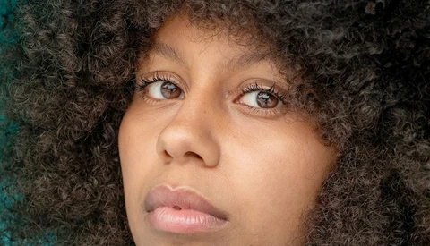 Portrait of a woman with curly dark hair looking upward with a contemplative expression.