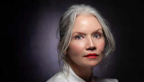 Portrait of a woman with gray hair and red lipstick against a dark background.