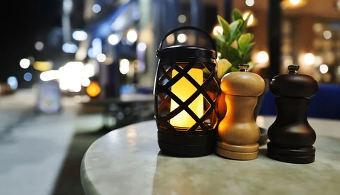 Black lattice lantern with glowing yellow light beside wooden salt and pepper mills on an outdoor table at night.