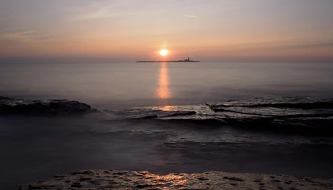 Sun setting over the ocean with a distant island silhouette and golden light reflecting on calm waves.