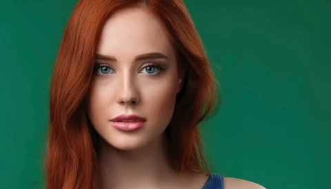 Woman with long reddish-brown hair and blue eyes against a solid green background.