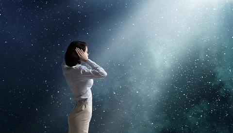 Woman in white shirt gazing upward amid falling particles and ethereal light rays.