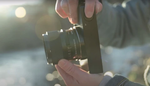 Photographer's hands holding a vintage manual focus lens against a blurred outdoor background in golden sunlight.
