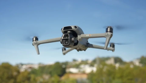 DJI Air 3 drone hovering in flight against blue sky with suburban landscape below.