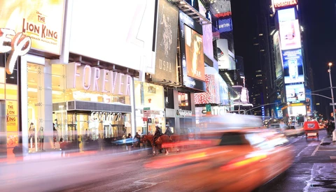 Times Square at night with blurred red taxi and illuminated billboards.