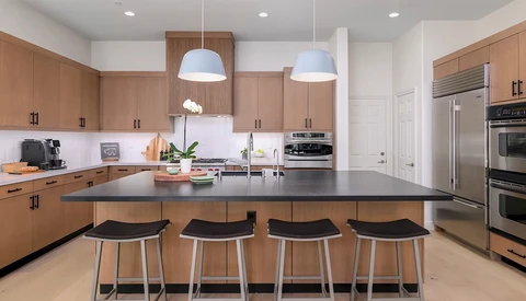 Modern kitchen with wood cabinetry, black island countertop, and four black bar stools under pendant lighting.