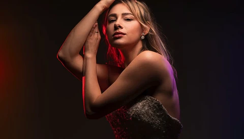 Woman posed against dark background with red and purple gel lighting.