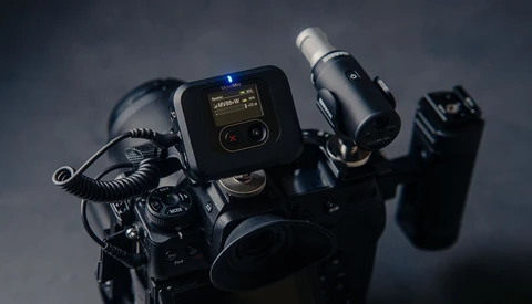 Professional cinema camera rig with mounted microphone, wireless transmitter, and monitor against dark background.