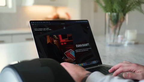 Laptop displaying a dark-themed portfolio website with red accents and photography imagery.
