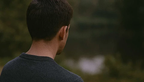 Man viewed from behind wearing a dark sweater, gazing toward blurred natural scenery.