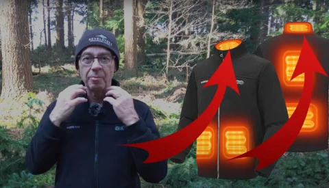 Man in dark jacket and beanie standing outdoors with forest background, demonstrating heated jacket with glowing thermal patterns illustrated with red arrows.