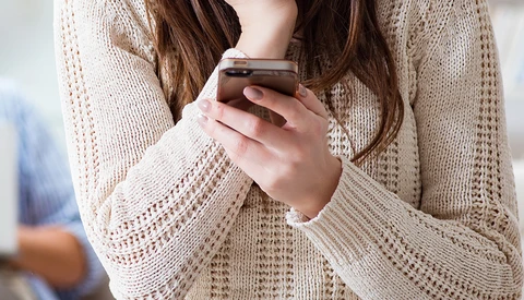 Person in cream knit cardigan holding a smartphone with both hands.