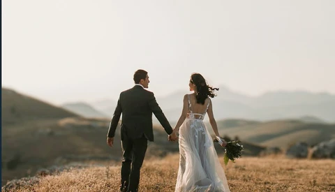 Bride and groom walking hand-in-hand through a golden harvest field at dusk.