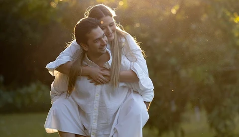 Man in white shirt giving piggyback ride to woman in golden-hour sunlight.