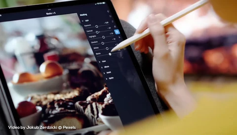 Photographer using stylus on tablet displaying food photography with adjustment panel open.