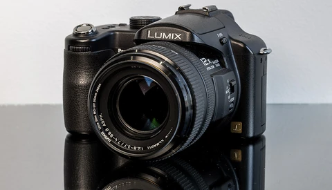 Panasonic Lumix digital camera with attached zoom lens on reflective surface.