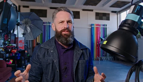 Bearded man speaking in a professional studio with professional lighting equipment visible.