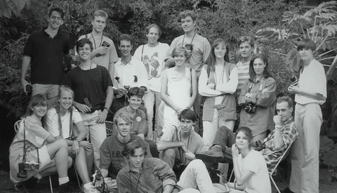 Black and white group portrait of approximately twenty people arranged in three rows outdoors among foliage.