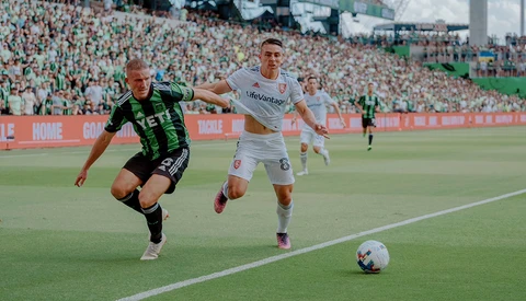 Two soccer players competing for the ball during a match in a crowded stadium.