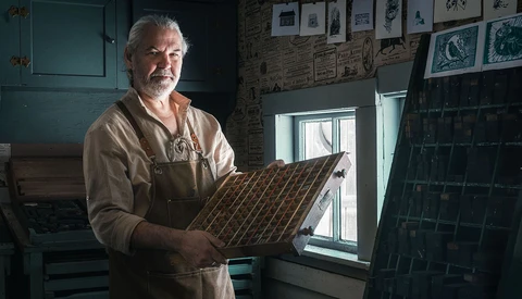 Craftsman holding a wooden sample board with diagonal wood grain pattern in his workshop.