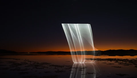 Light painting over a still body of water at dusk with warm orange sky and dark shoreline silhouettes.