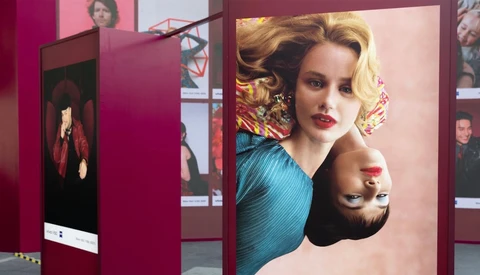 Exhibition display panels with portrait photographs and warm pink-toned lighting against burgundy walls.