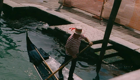 Gondolier in striped shirt standing in gondola at dock, preparing boat or waiting for passengers.