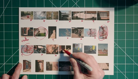 Contact sheet of architectural and landscape photographs laid flat on a cutting mat with hands marking selections in red.