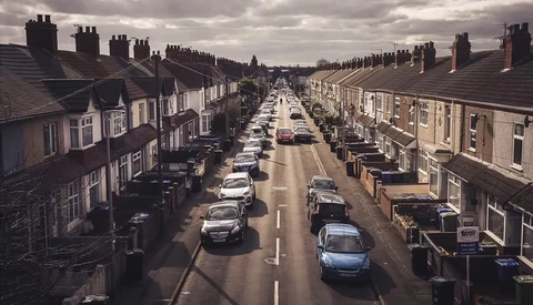 Overhead view of a residential street lined with parked cars and terraced houses under overcast sky.