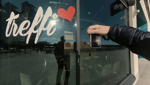Hand reaching toward a glass storefront door with "hello" text and red heart decal.