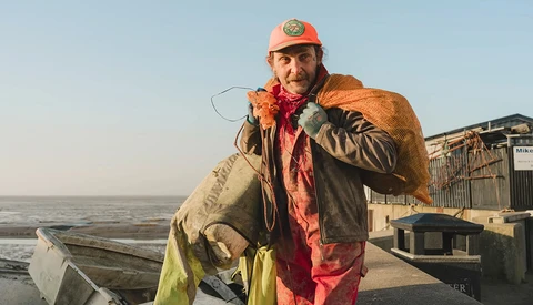 Commercial fisherman holding large caught fish at a harbor dock at sunrise.