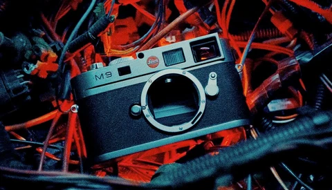 Leica M9 rangefinder camera body positioned on vibrant red and blue neon-lit cables and wires.