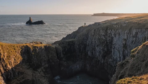 Dramatic coastal cliffs at golden hour with a sea stack and distant headlands across calm waters.