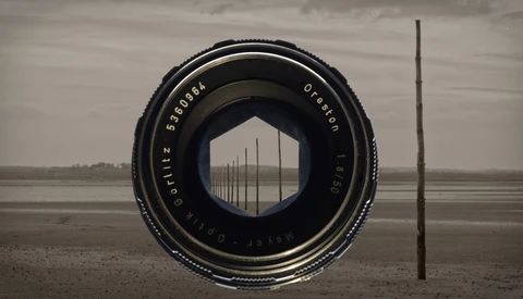 Vintage camera lens framing a row of utility poles stretching across a flat, desolate landscape under overcast sky.