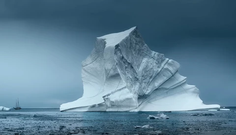 Massive iceberg with dramatic angular formations floating in dark blue ocean water.