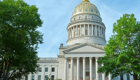 Classical government building with white columns and gold dome framed by green trees.