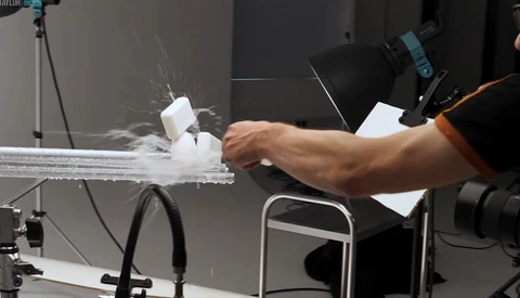 Photographer's hand adjusting a product on a white platform during a studio shoot with key lighting setup.