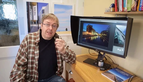 Photographer in plaid shirt at desk reviewing architectural images on dual monitors.