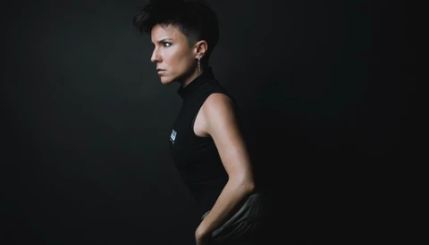 Person in black sleeveless top photographed in profile against dark background.