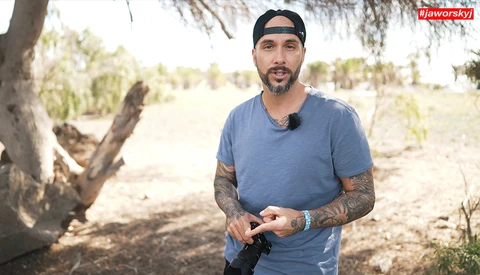 Man in blue t-shirt and headband standing outdoors holding camera equipment.