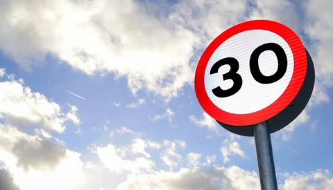 Street speed limit sign showing 30 kilometers per hour against a blue sky with white clouds.
