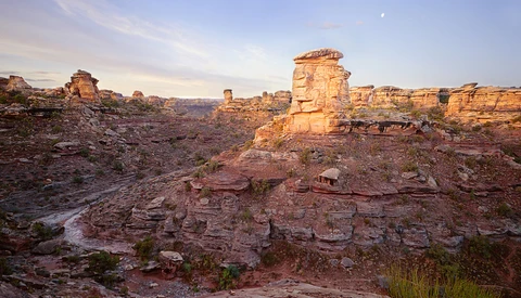 Golden-hour sunlight illuminates layered sandstone formations and rock outcroppings in an arid canyon landscape.