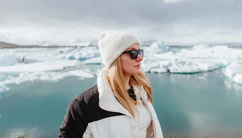 Woman in winter clothing overlooking a glacial lake filled with icebergs.