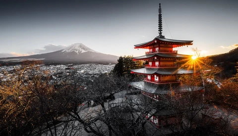 Red pagoda silhouetted against snow-capped mountain at sunset with golden light breaking through.