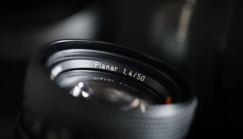 Close-up of a Planar 1.4/50mm lens with shallow depth of field and dramatic lighting against a dark background.
