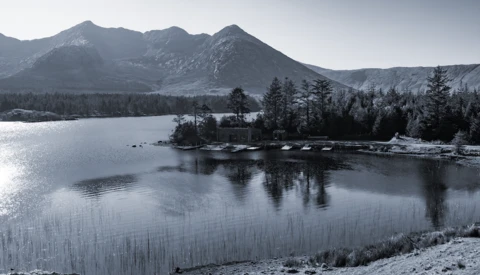 Snow-covered mountains and coniferous forest reflected in a partially frozen alpine lake.