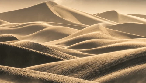 Undulating sand dunes with dramatic warm lighting and deep shadows creating sculptural forms.