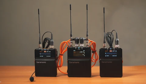 Three Saramonic wireless microphone transmitter units arranged on a wooden surface with cables and antennas.