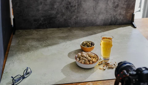 Styled flat lay with nuts, olives, juice, and eyeglasses on a concrete surface.