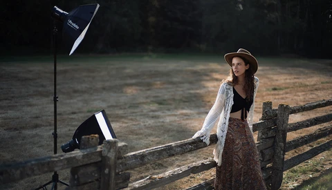 Woman posing by wooden fence with studio lighting setup including reflector and off-camera flash.